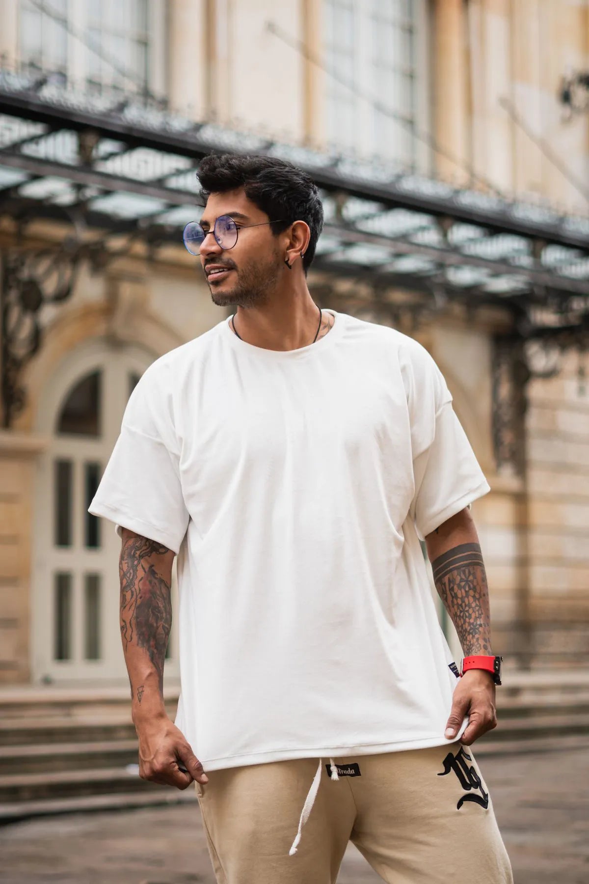 Man wearing a white t-shirt and beige pants standing outdoors with a building in the background