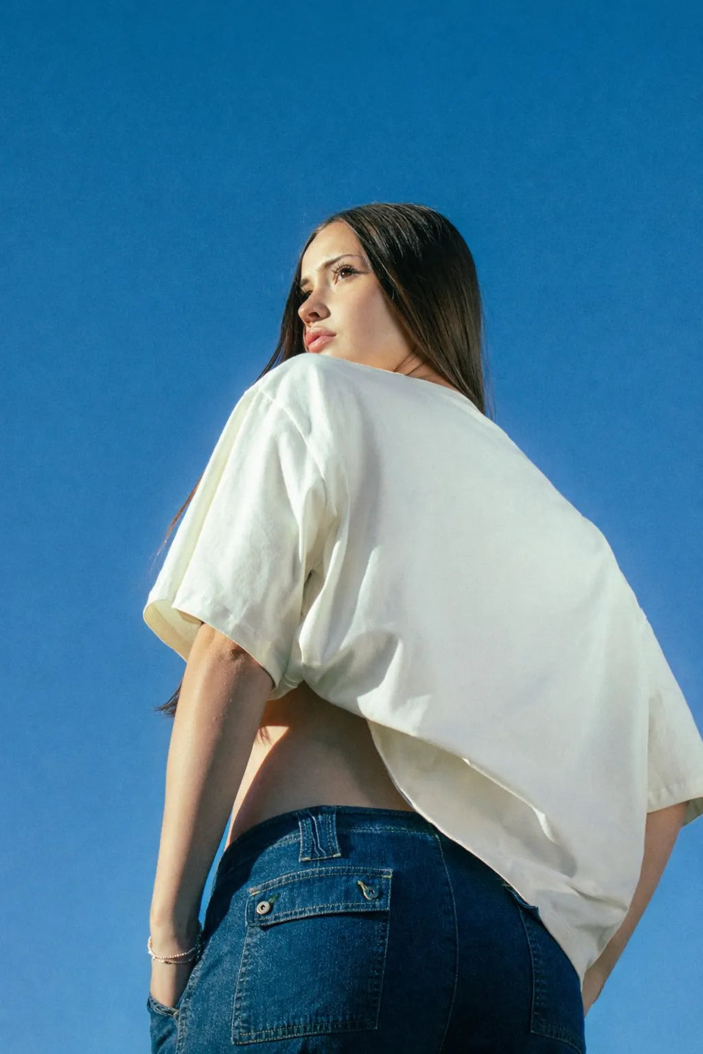 Woman wearing a white top and blue jeans against a clear blue sky