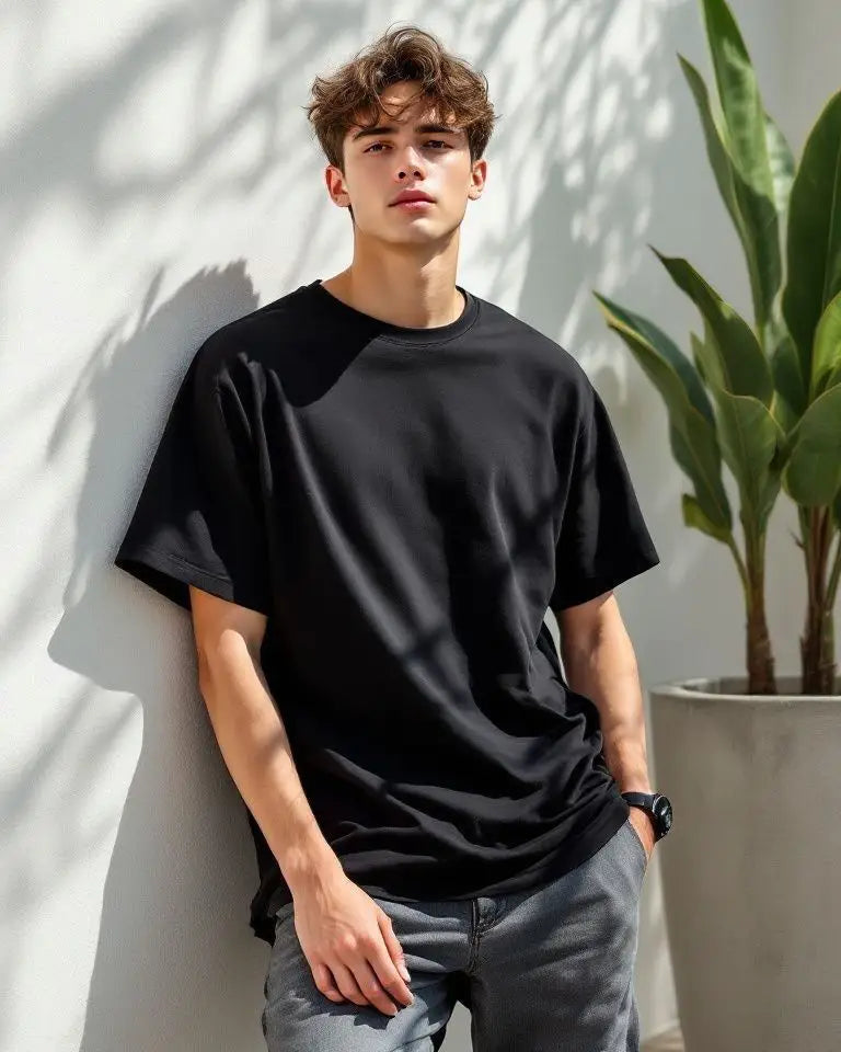 Man wearing a black t-shirt against a white wall with a plant in the background